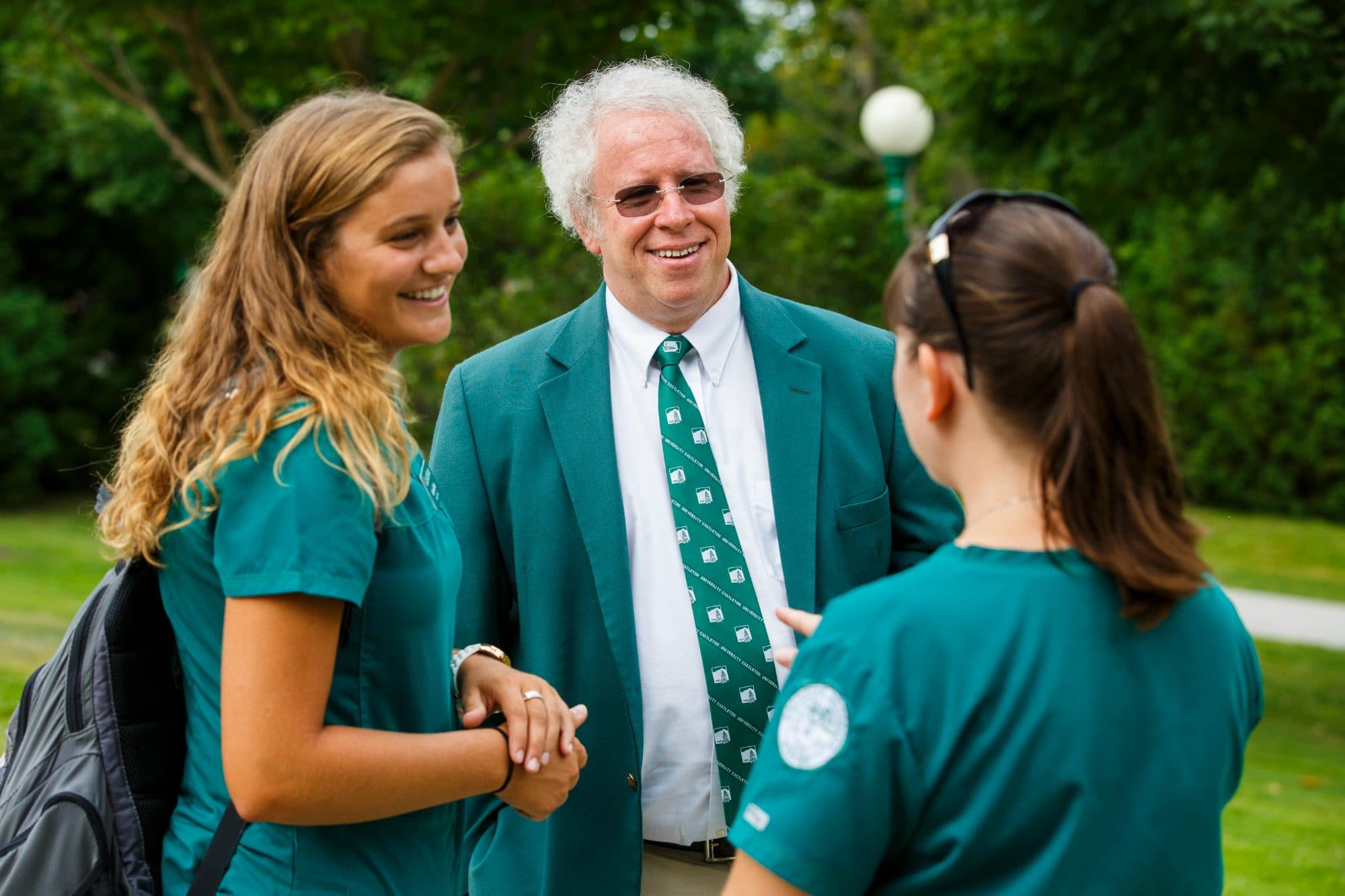 Dave Wolk greeting two students outdoors on the Castleton green.