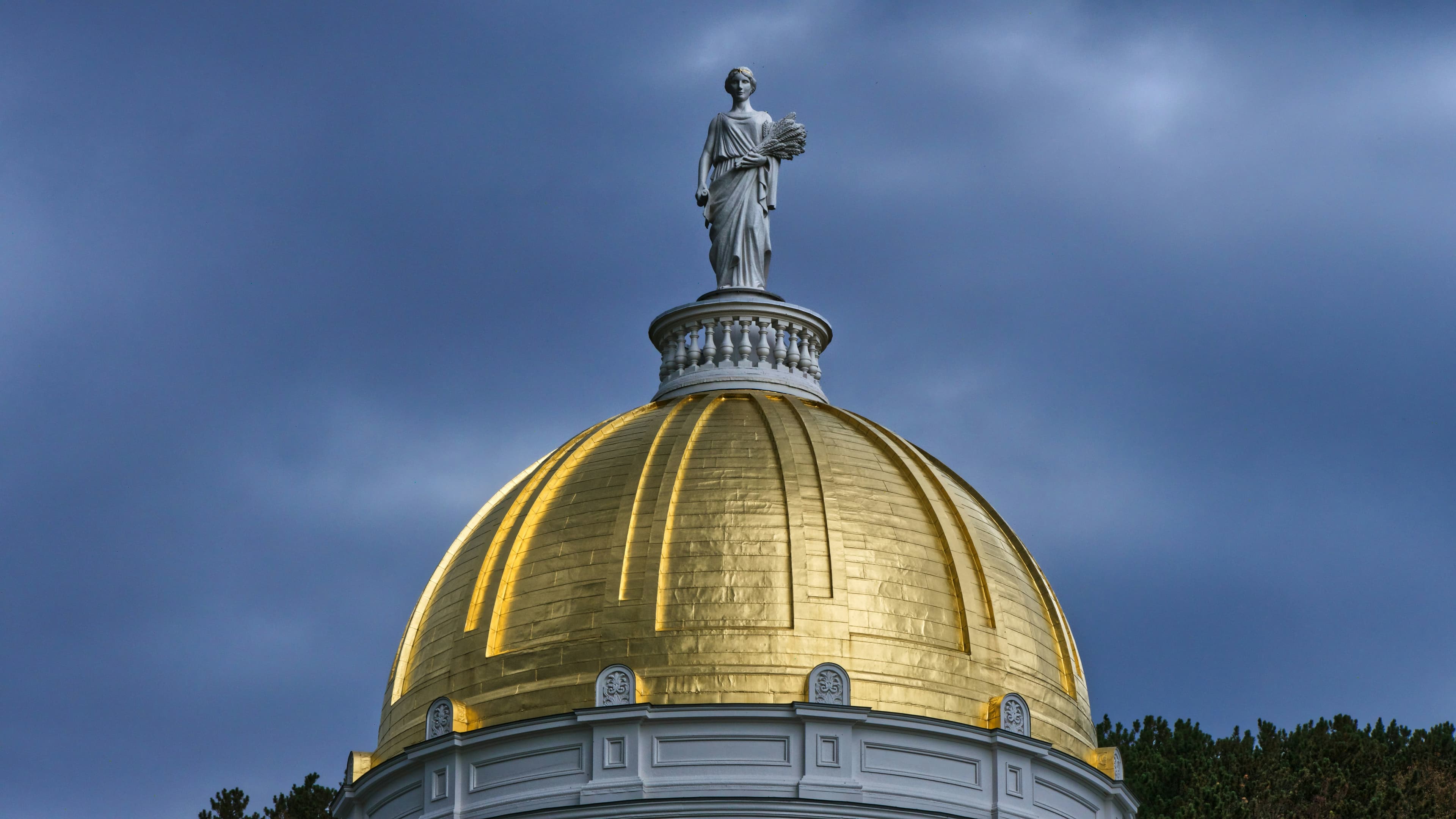 The gilded dome of the Vermont State House in Montpelier against a dusk sky.