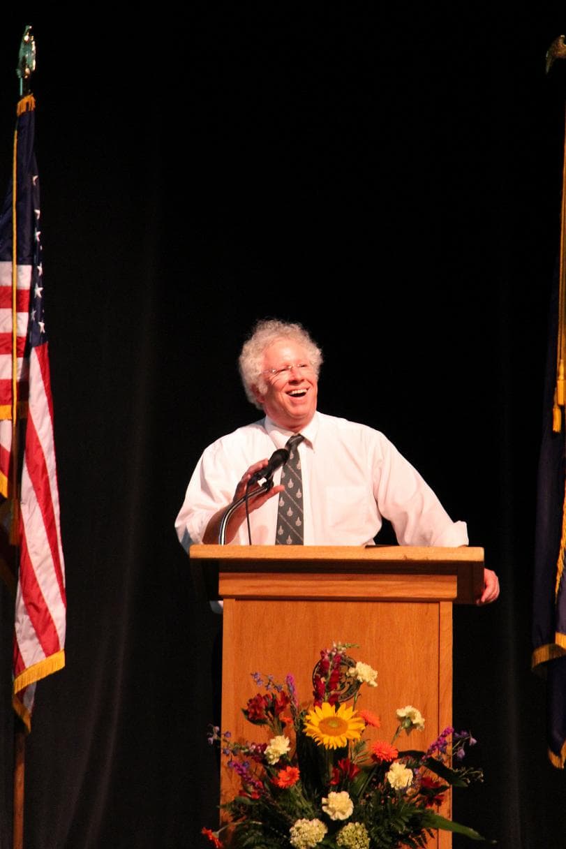 Dave Wolk laughing mid-speech at a podium with American and Vermont flags.
